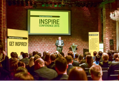 Sprecher steht vor Publikum bei der INSPIRE CONFERENCE 2015 in einem Saal mit Backsteinwand.
