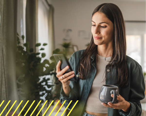 Woman holding smartphone and mug looking at the screen in a living room