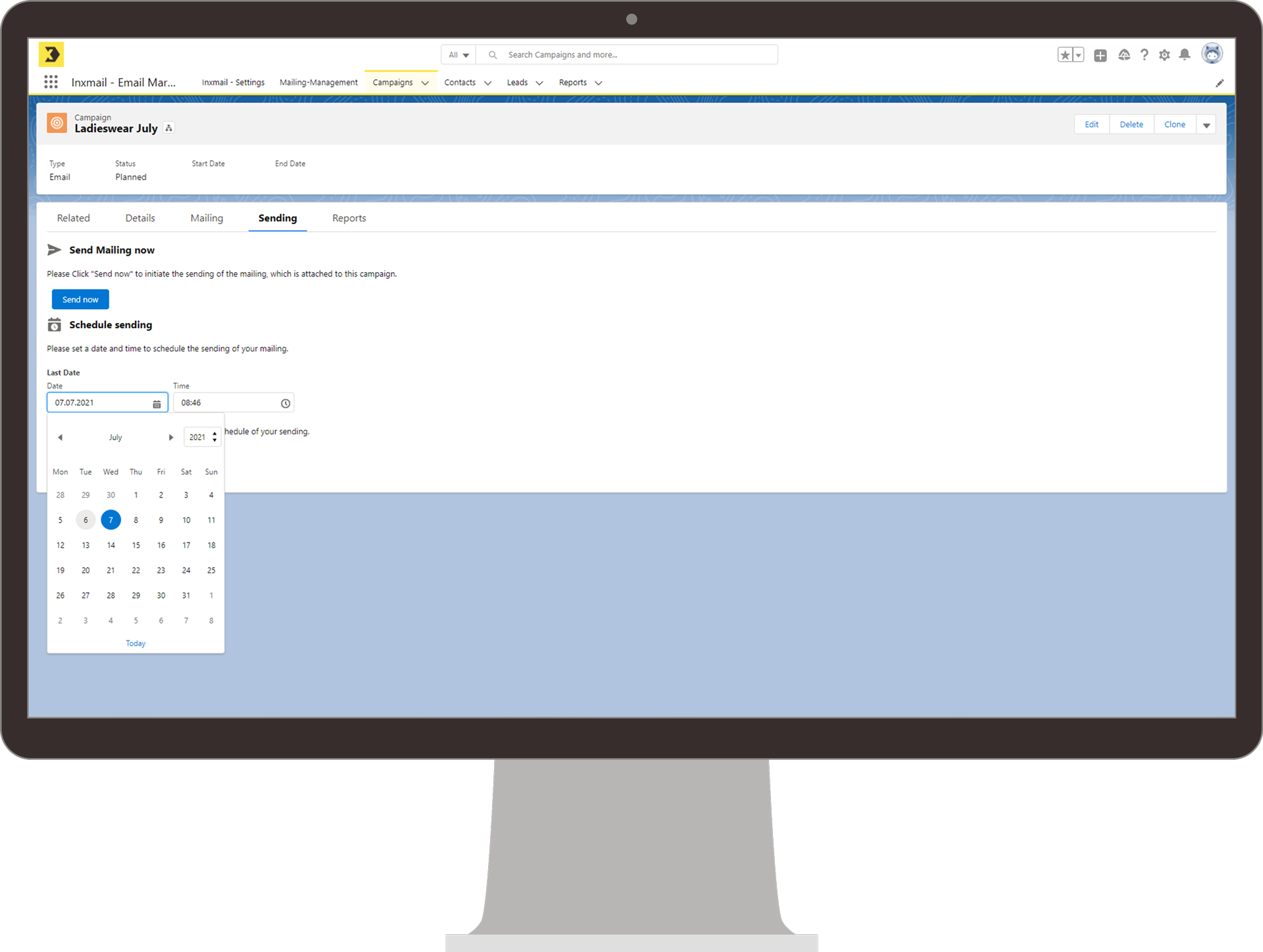 Ein Monitor zeigt die Inxmail-Integration in Salesforce auf der „Send“-Seite einer E-Mail-Kampagne mit dem Titel „Ladieswear July“. Die Benutzeroberfläche bietet die Option, das Mailing sofort zu versenden oder den Versand zu einem späteren Zeitpunkt zu planen. Ein Kalender zur Auswahl des Versanddatums ist geöffnet.